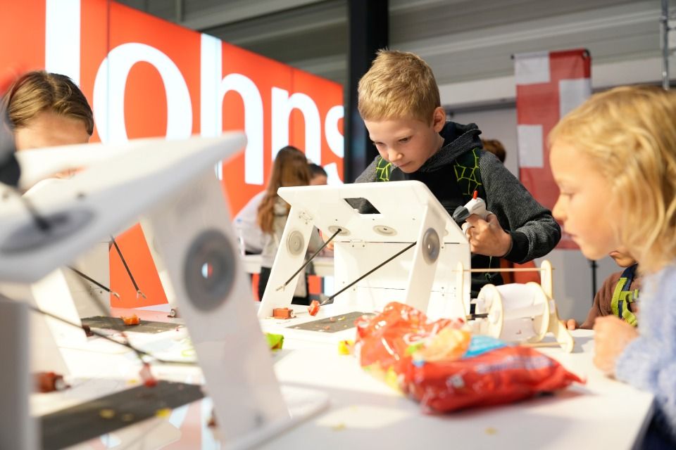 Kinder arbeiten in einer Werkstatt an einem weissen Tisch an einem Projekt.