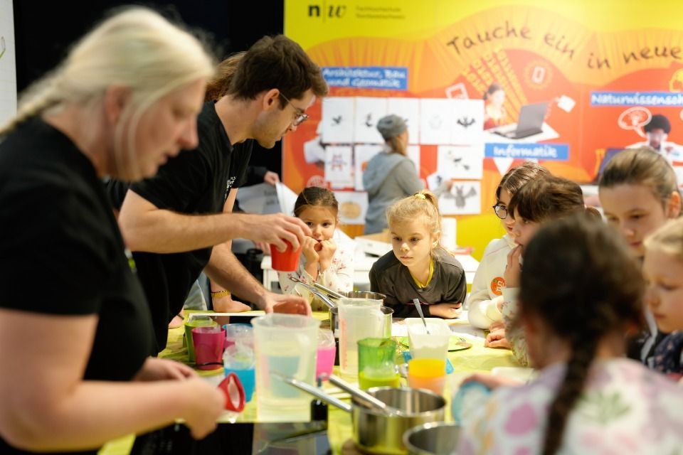 Menschen, darunter auch Kinder, führen an einem Tisch ein wissenschaftliches Experiment durch.