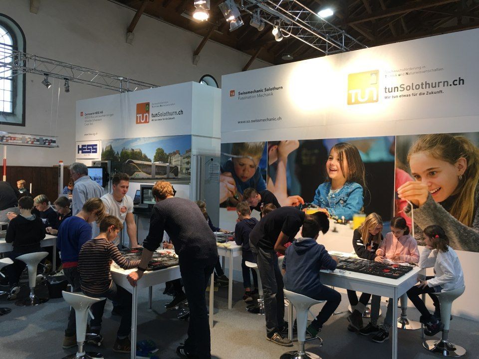 Kinder und Erwachsene interagieren an einem Stand mit Computern.