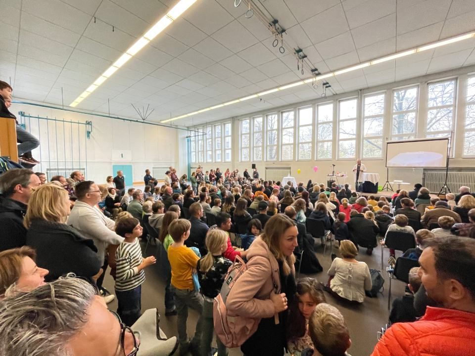 Eine grosse Menschenmenge hat sich in einem Raum versammelt und starrt auf eine Bühne.