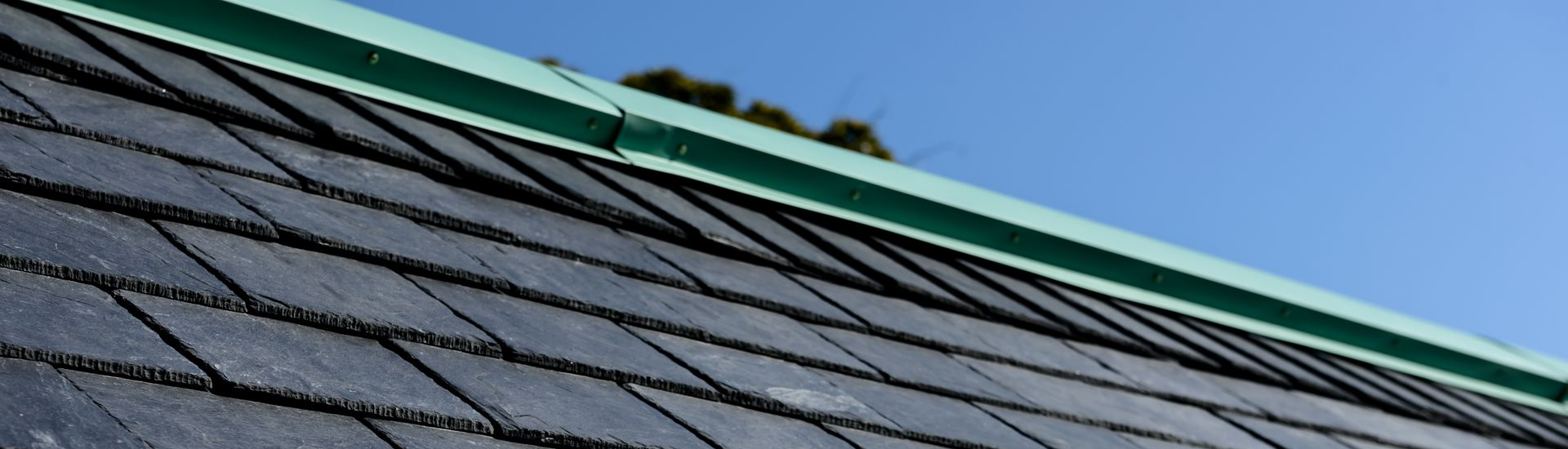 Vue d'un toit aux bardeaux gris foncé et à bordure verte, se détachant sur un ciel bleu.