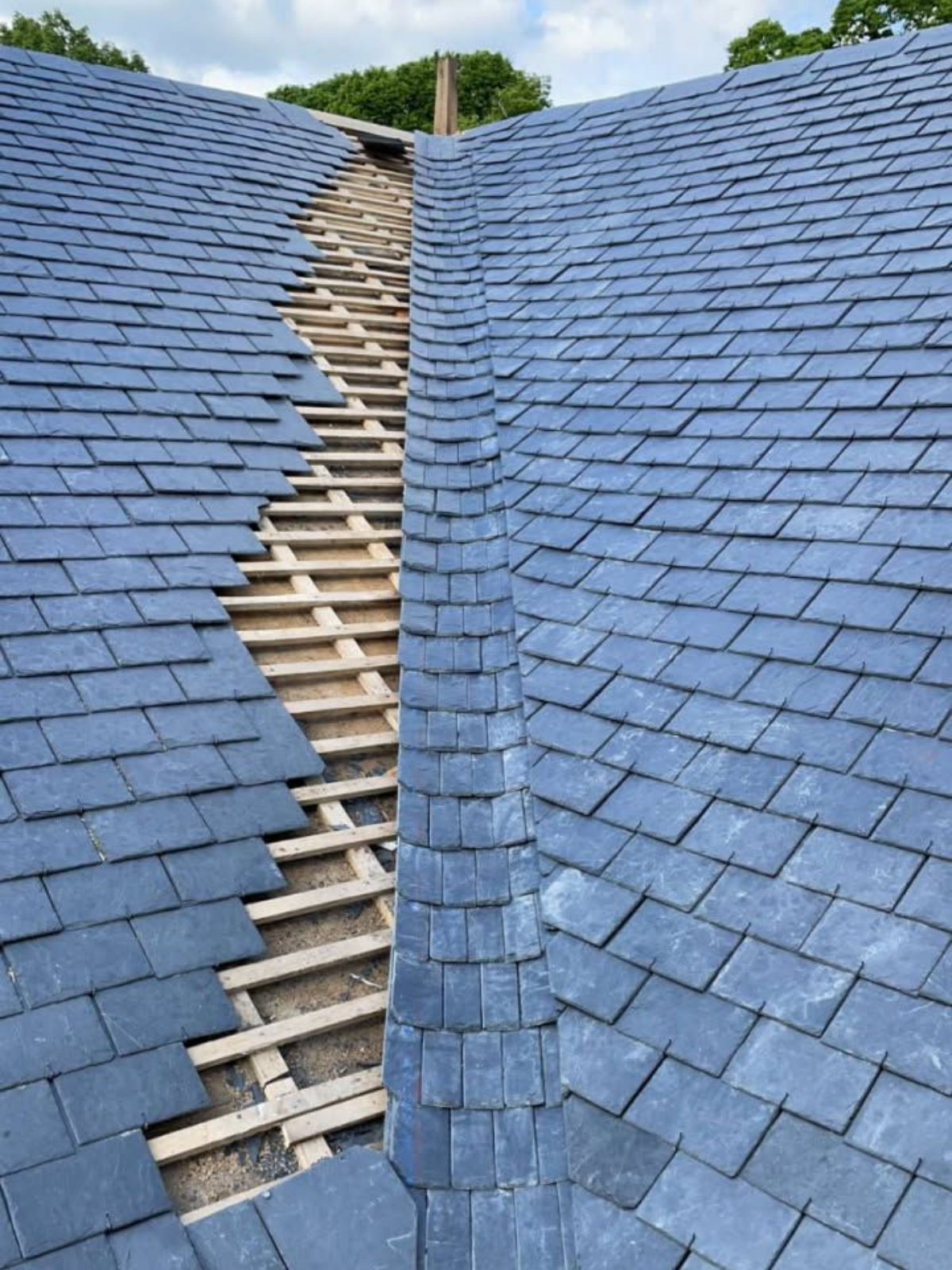 Un toit en ardoise bleue, partiellement démonté, laissant apparaître une charpente en bois.