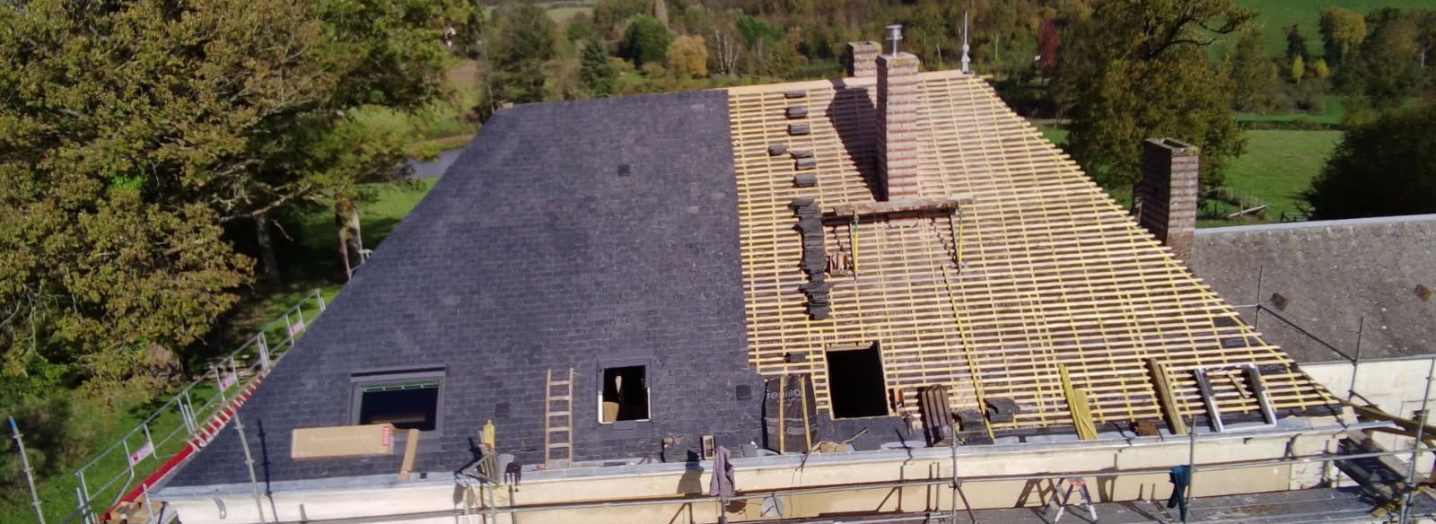 Toiture en construction, moitié recouverte de bardeaux noirs, l'autre moitié laissant apparaître la charpente en bois.