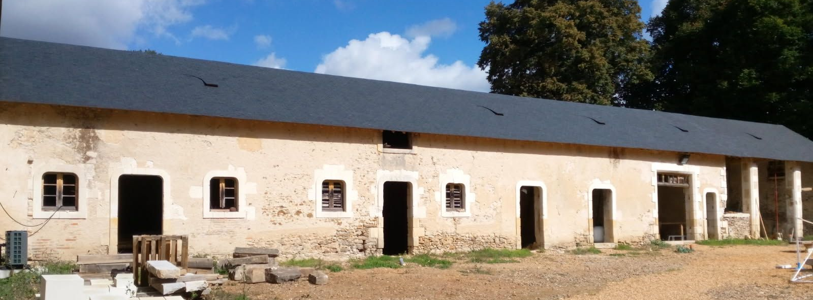 Bâtiment long et clair, au toit sombre et percé de multiples ouvertures. Situé en milieu rural.