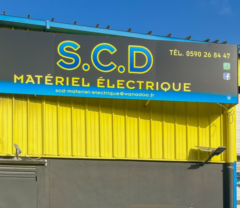 Enseigne bleue de façade au-dessus d'un auvent jaune et d'un mur gris.