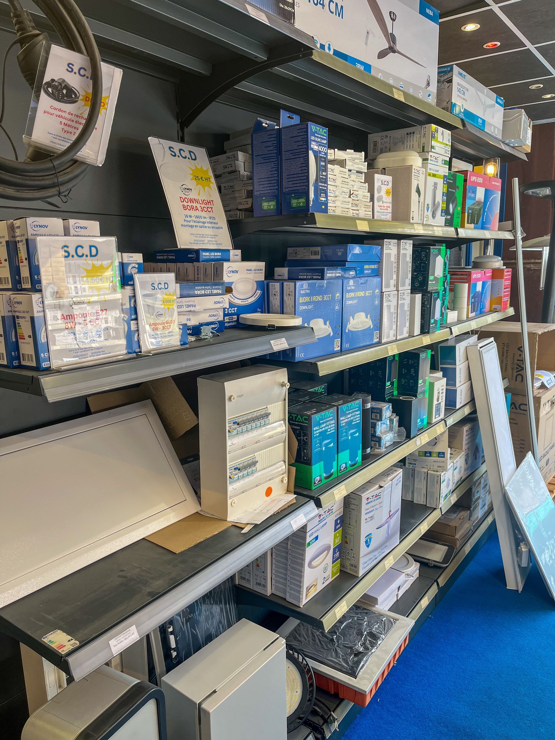 Des rayons de magasin regorgent de produits en boîte et d'articles de toilette assortis, dans une allée recouverte de moquette bleue.