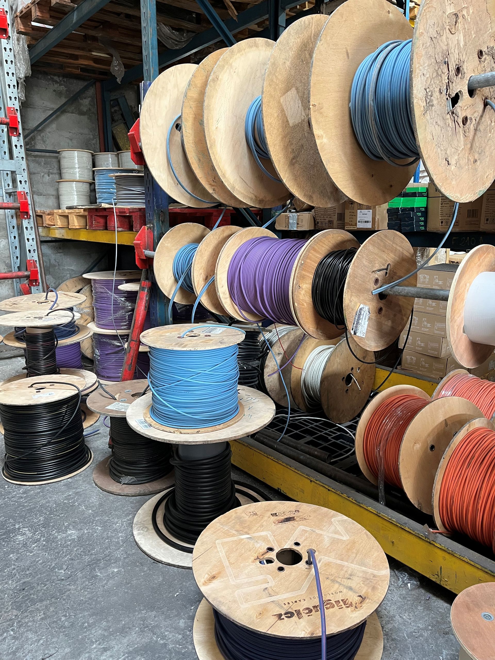 Des bobines de cordes et de fils colorés empilées dans une allée d'entrepôt industriel.