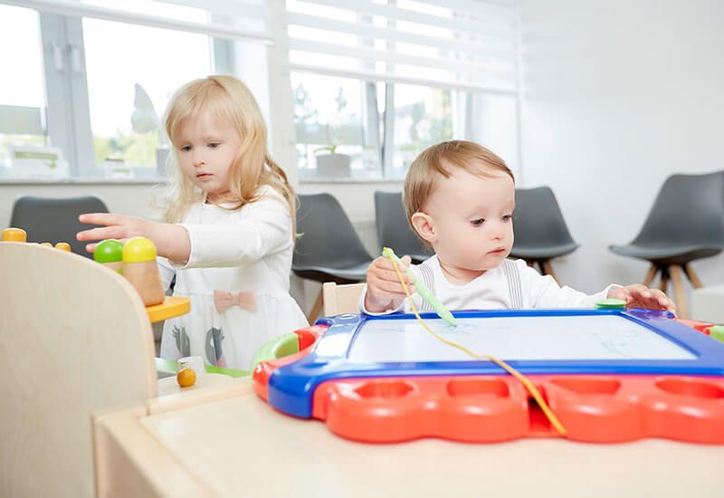 Zwei Kleinkinder spielen in einem hellen Zimmer mit buntem Spielzeug.