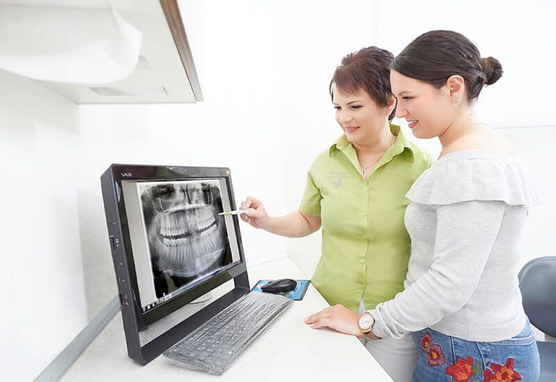 Zwei Frauen betrachten in einer Klinik ein zahnärztliches Röntgenbild auf einem Computerbildschirm.
