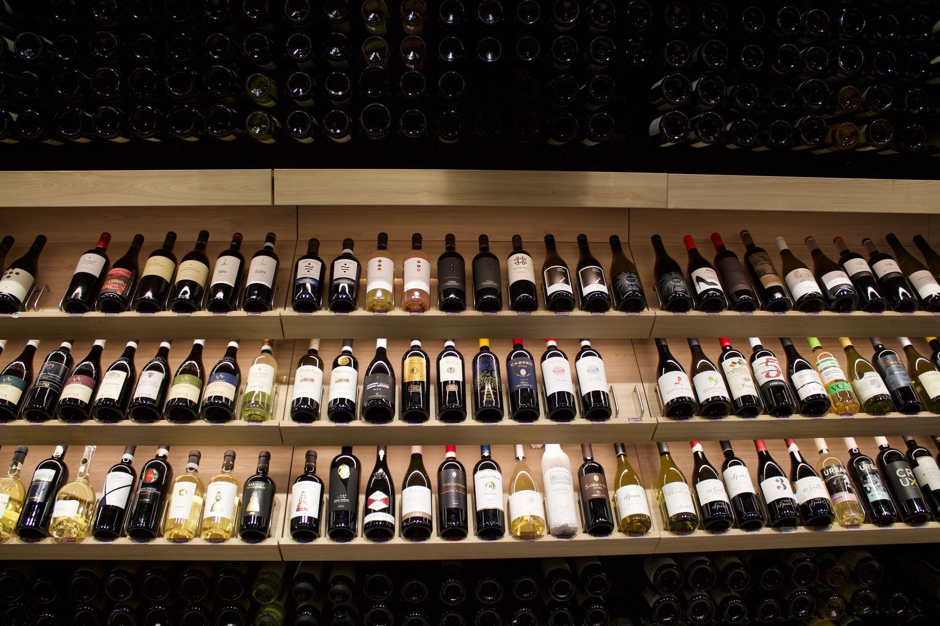 Des rangées de bouteilles de vin exposées sur des étagères en bois dans un cadre faiblement éclairé évoquant une cave.