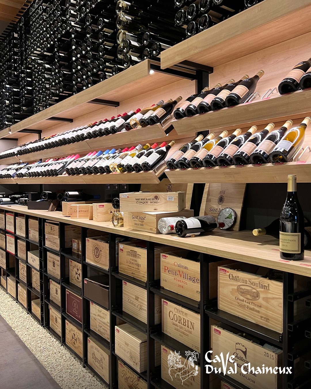 Présentoir à vins dans un magasin, avec des bouteilles sur des étagères inclinées et des cubix empilés en dessous.