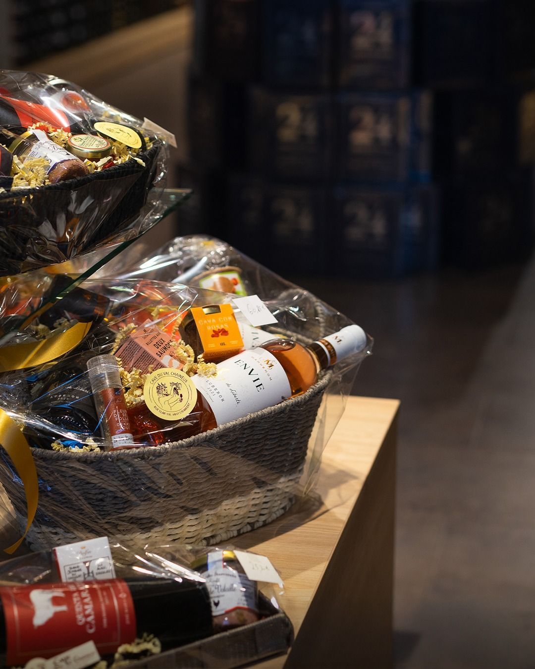 Des paniers cadeaux contenant des bouteilles et des en-cas emballés sont présentés sur une table en bois.