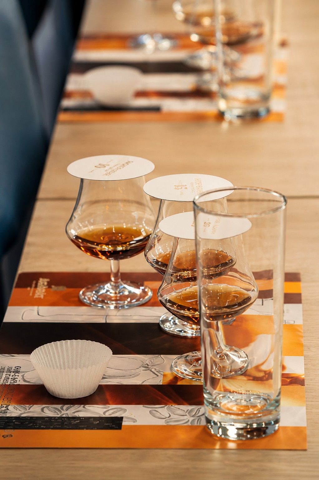 Deux verres à whisky et un gobelet sont posés sur un set de table rayé, au comptoir d'un bar.