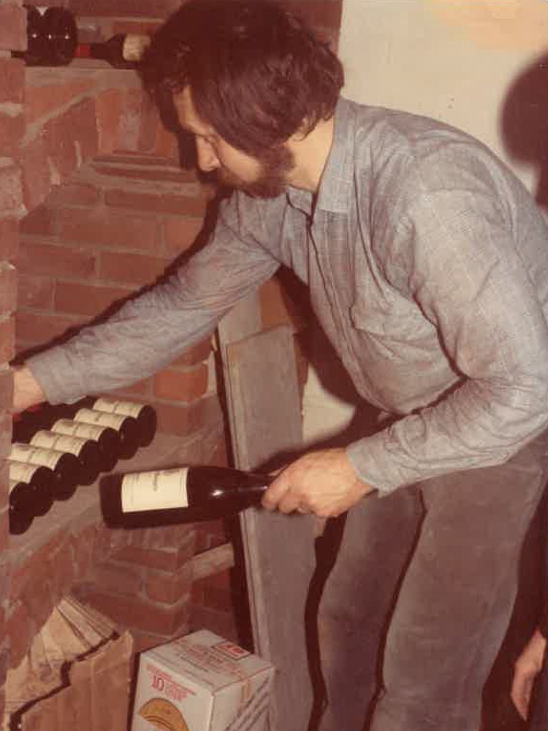 Une personne range des bouteilles de vin dans un casier à vin encastré dans un mur de briques d'une cave