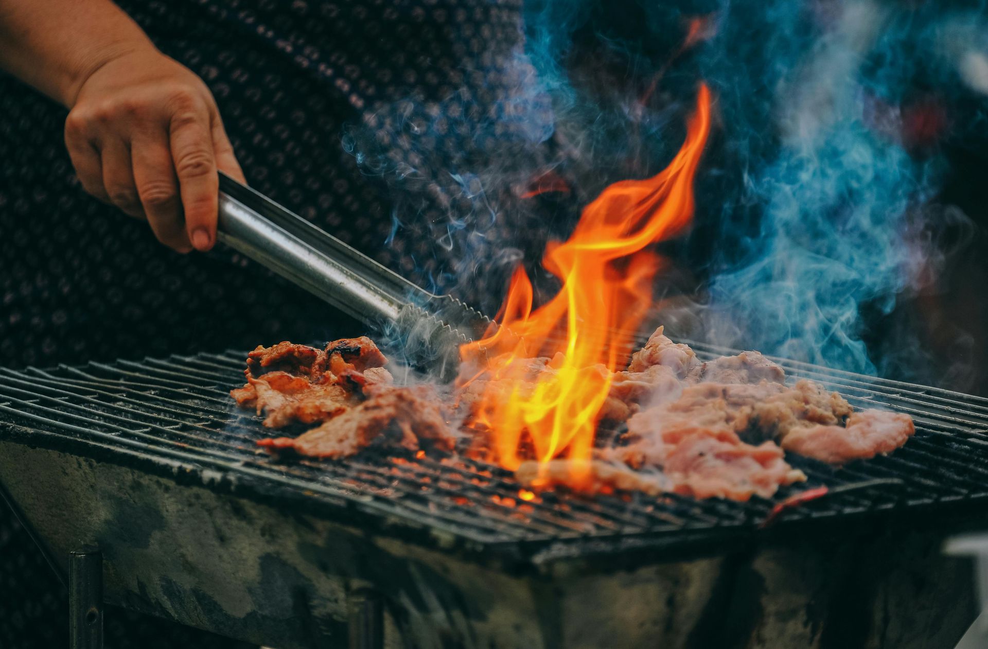 Retourner à la main de la viande grillée avec des pinces au-dessus des flammes chaudes et de la fumée d'un barbecue
