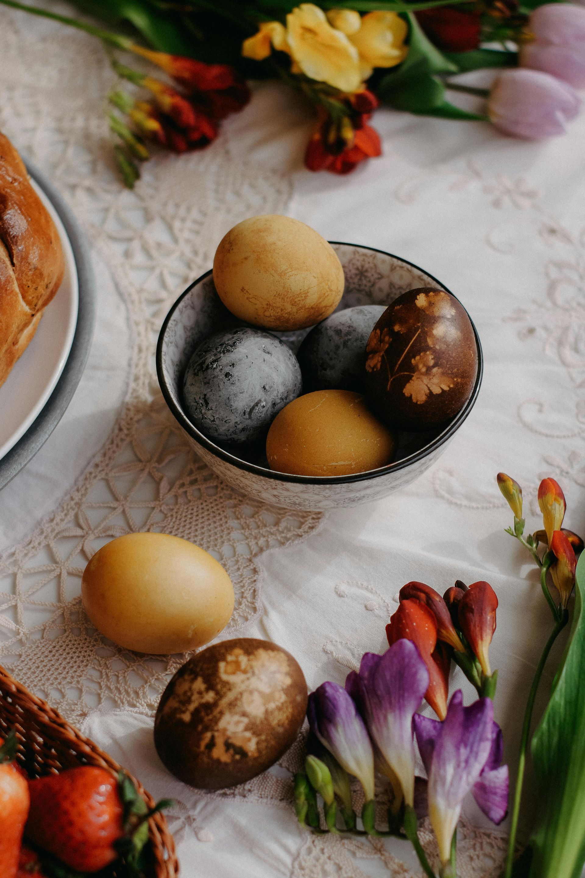 Des œufs de Pâques décorés dans un bol avec des fleurs sur une table rustique