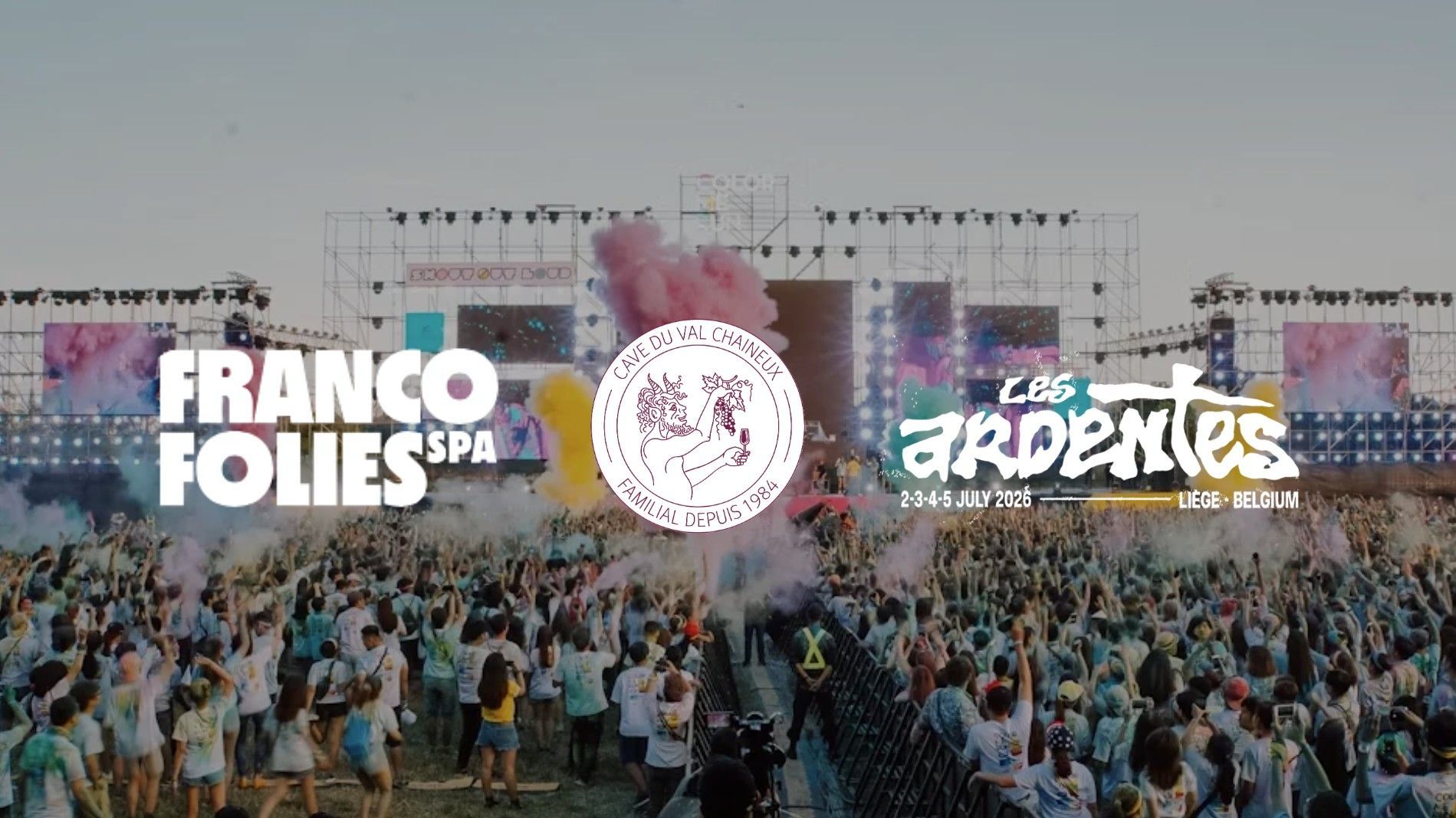 Foule à un festival de musique en plein air avec scène, fumée colorée et logos de l'événement superposés.