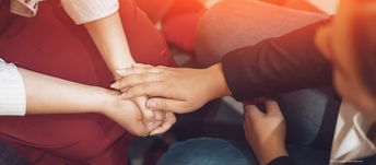 Person legt anderer Person Hand auf die gefalteten Hände