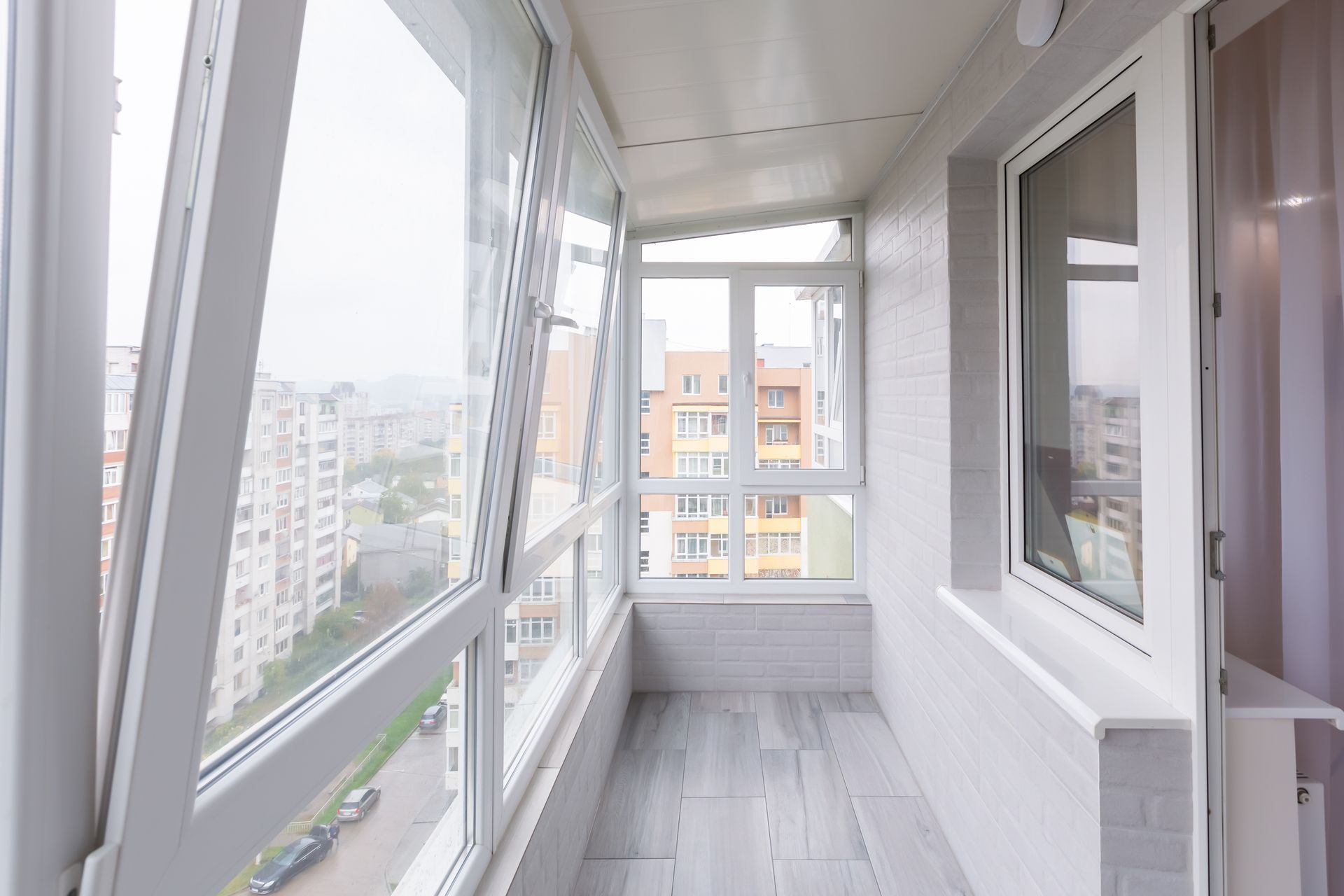 Balcon lumineux et fermé avec baies vitrées et vue sur les immeubles de la ville