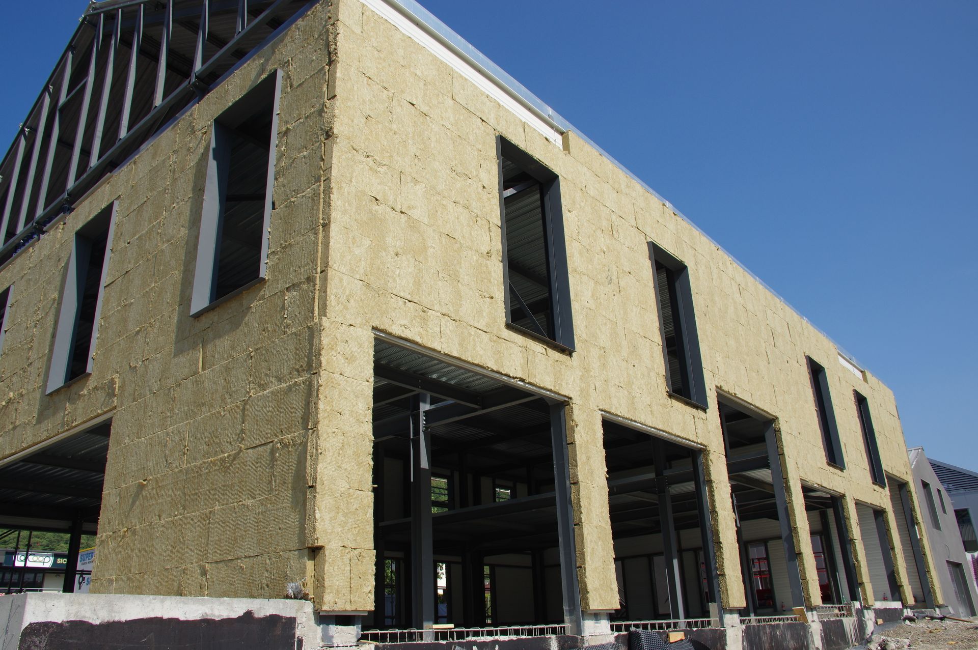 Bâtiment beige partiellement fini avec de grandes ouvertures de fenêtres et une charpente apparente