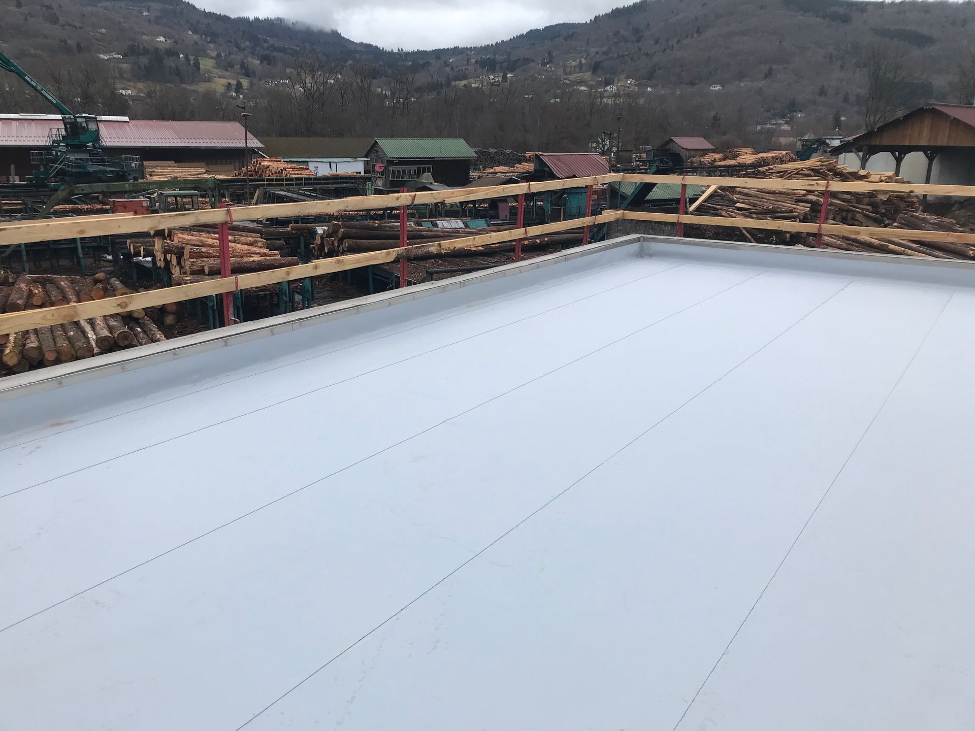Grand toit blanc sur un chantier de construction en zone rurale, avec des bâtiments et des collines en arrière-plan