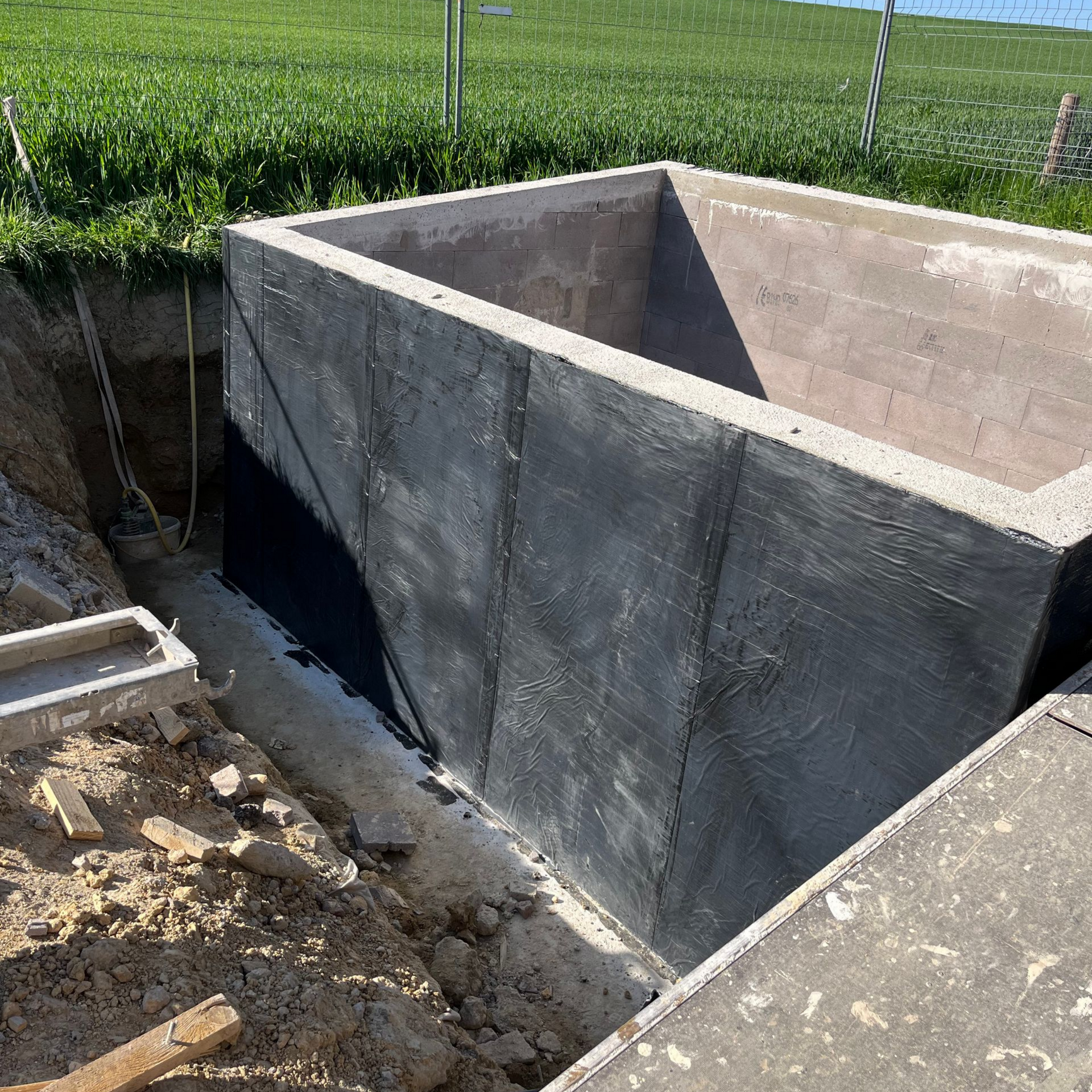 Un réservoir souterrain en béton est en construction à côté d'un champ herbeux et de terre excavée