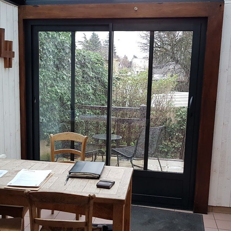 Des portes coulissantes en verre s'ouvrent sur une cour arrière. À l'intérieur, une table et des chaises en bois sont installées.
