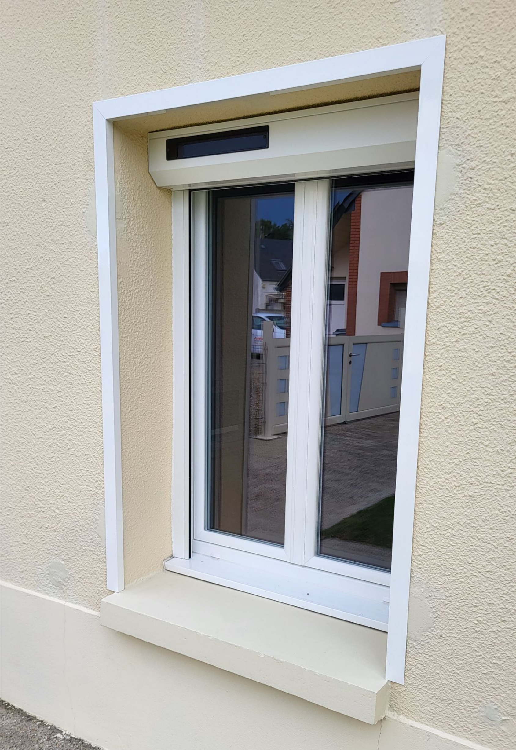 Fenêtre avec volets blancs fermés et cadre sur une façade beige.