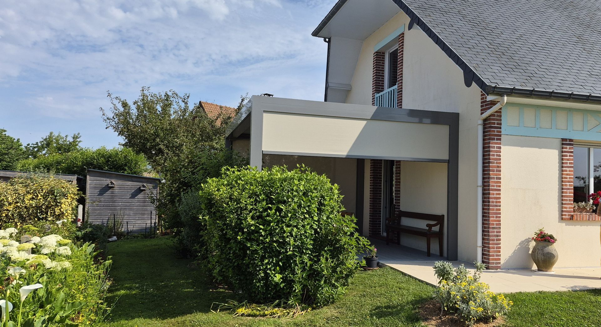 Pergola extérieure beige avec murs blancs, table et plantes vertes.