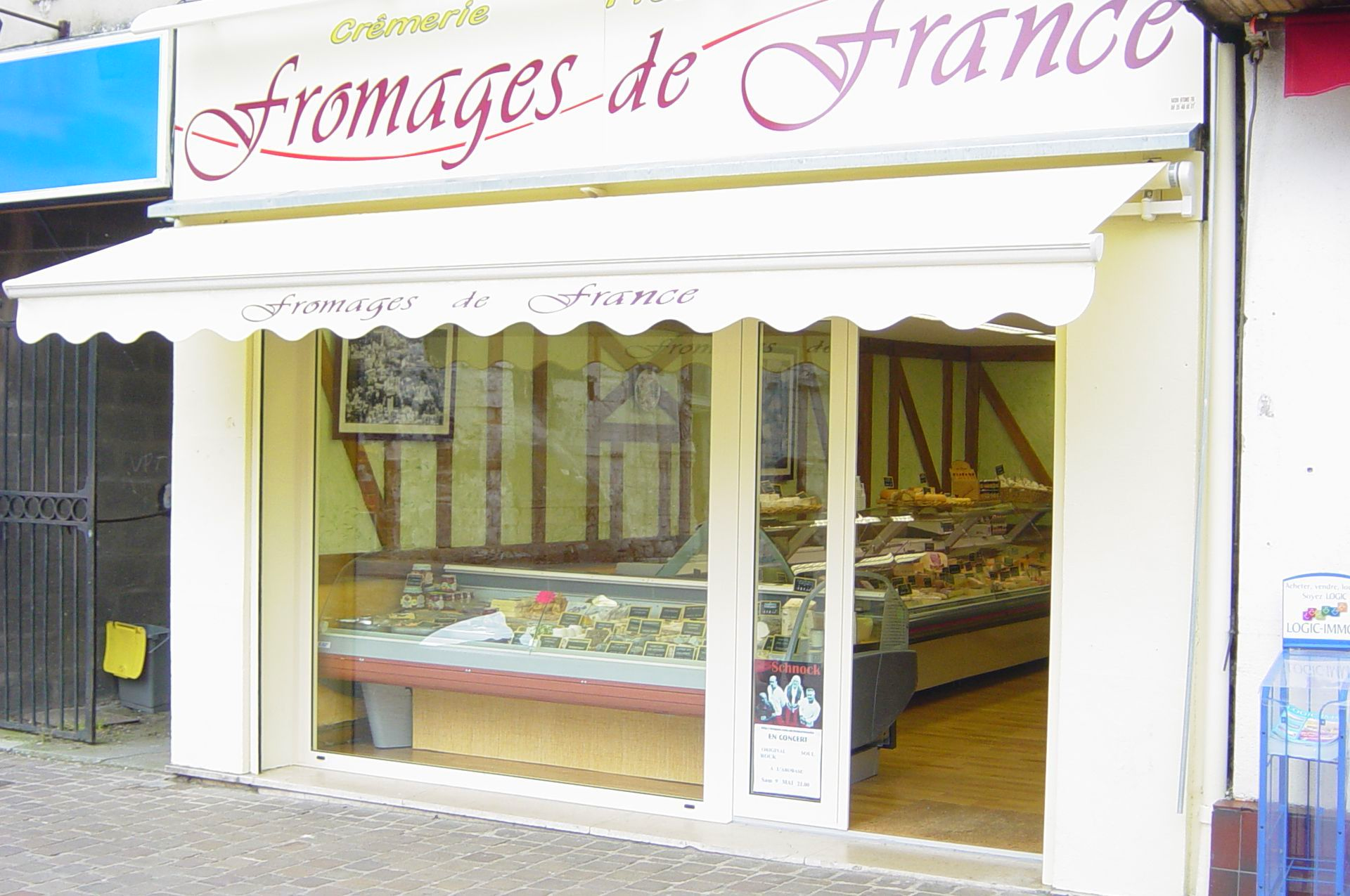 Extérieur d'une fromagerie française, auvent couleur crème, vitrine avec fromages, enseigne indiquant « Fromages de France ».
