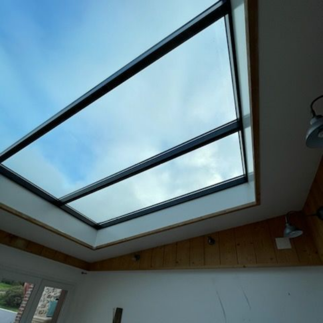 Puits de lumière dans une pièce donnant sur un ciel bleu nuageux. Cadre noir, moulures en bois, murs blancs.