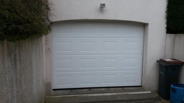 Porte de garage blanche à panneaux encastrés, intégrée à un mur blanc avec marches.
