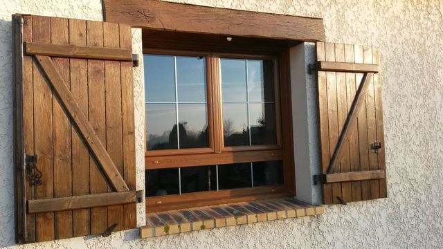 Volets en bois sur une fenêtre à cadre marron, encastrée dans un mur en stuc blanc.