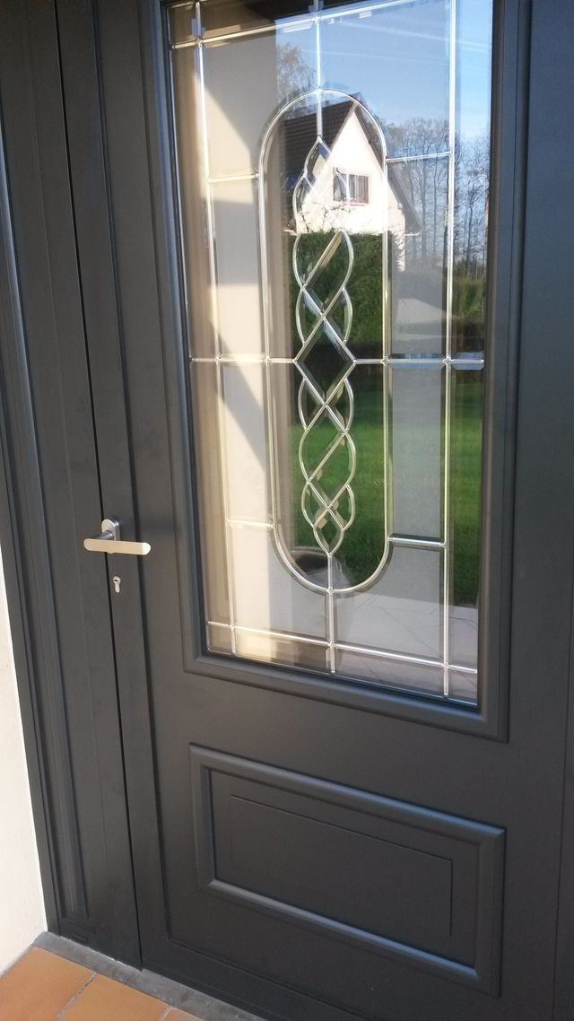 Porte d'entrée gris foncé avec panneau de verre, poignée argentée et motif décoratif en verre.