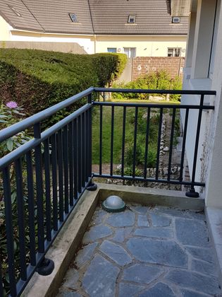 Petit balcon avec rambarde en métal noir, sol en pierre et vue sur la verdure.