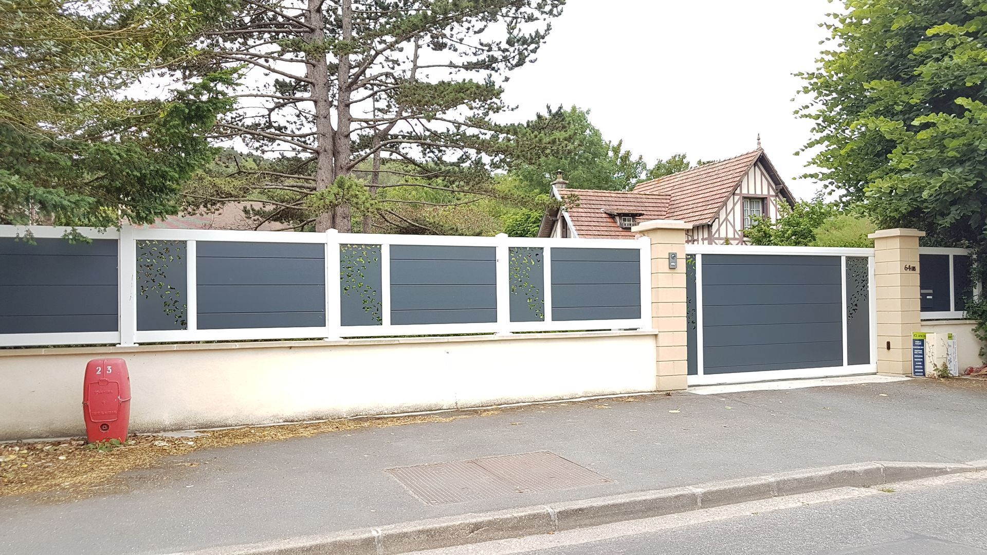 Clôture grise et blanche avec portail assorti, devant une maison, vue depuis la route.