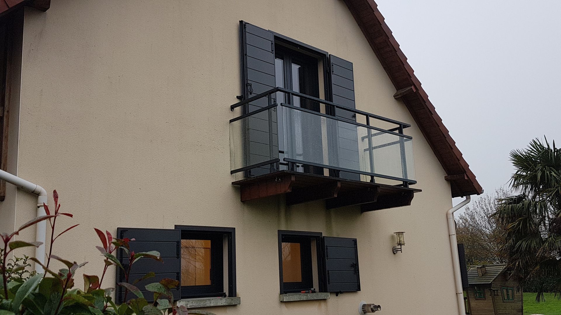 Extérieur de la maison avec un petit balcon et des volets noirs.