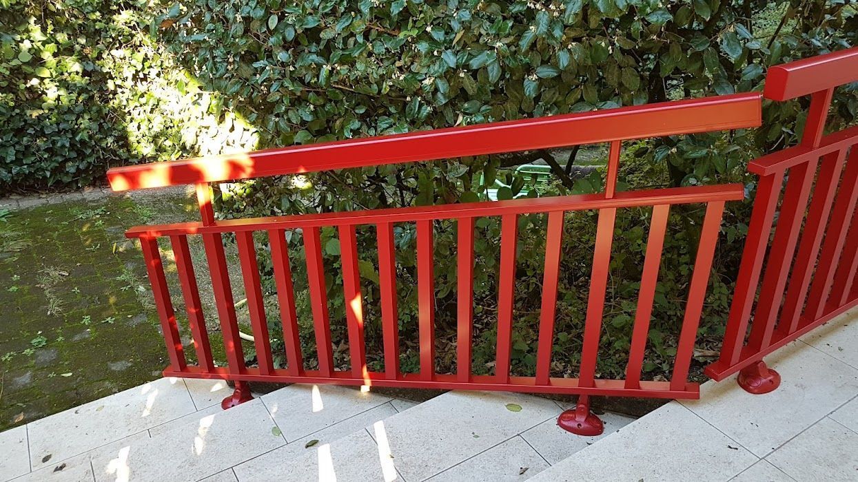 Rambarde en bois rouge sur des marches en béton, sur fond de verdure.