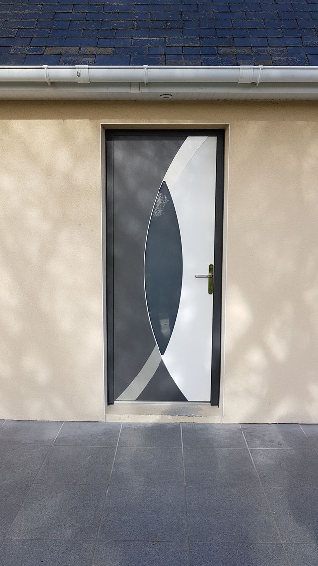 Porte d'entrée à motif géométrique gris et blanc, encastrée dans un mur beige, sous un toit foncé.