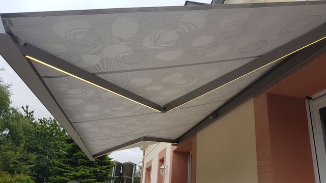 Auvent à motifs gris et blancs s'étendant depuis un bâtiment, avec éclairage intégré.