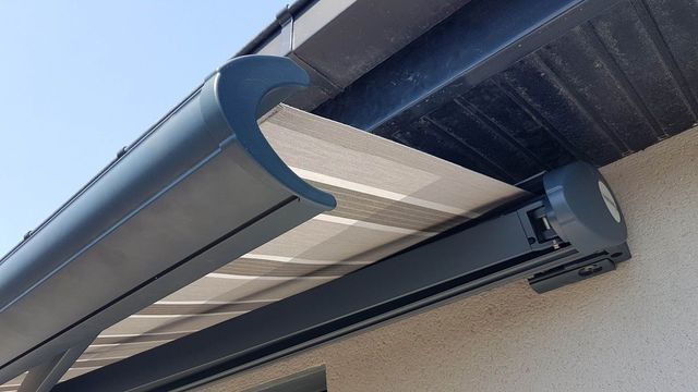 Auvent rétractable gris fixé à la façade d'un bâtiment, partiellement déployé pour offrir de l'ombre.