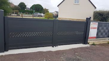 Portail coulissant gris foncé avec partie supérieure à motifs, devant une maison.