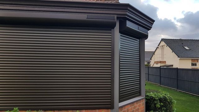 Des volets roulants brun foncé recouvrent les fenêtres d'un angle d'immeuble en briques, vue extérieure.