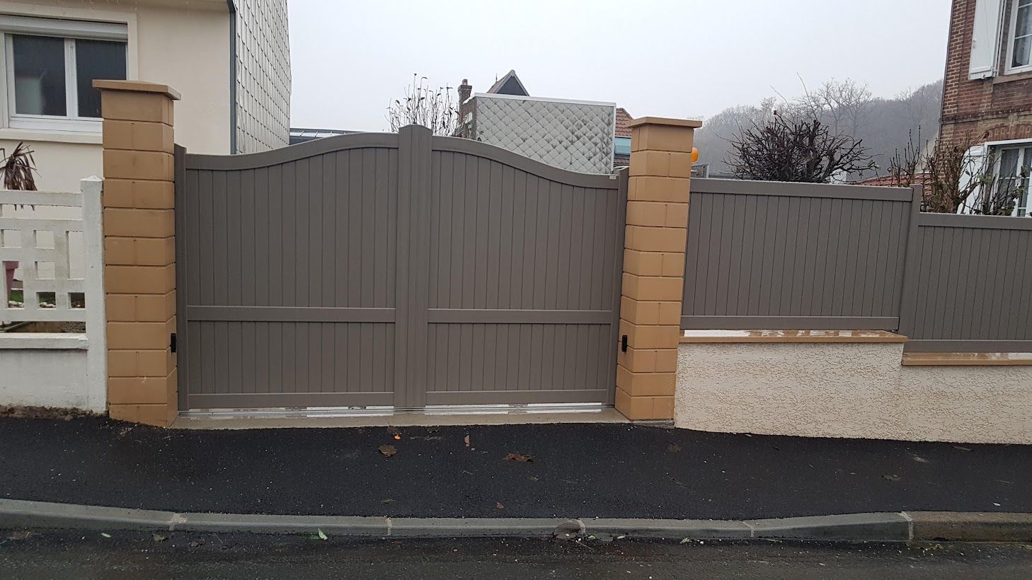 Portail double gris avec clôture et piliers en briques assortis.