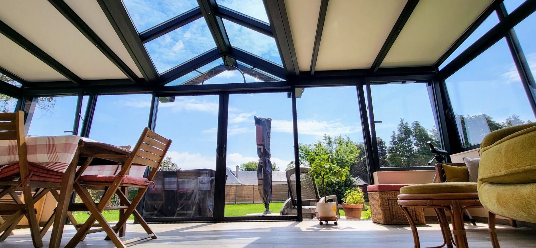 Intérieur d'une véranda avec table et chaises. Vue sur l'extérieur ensoleillé. Canapé jaune.