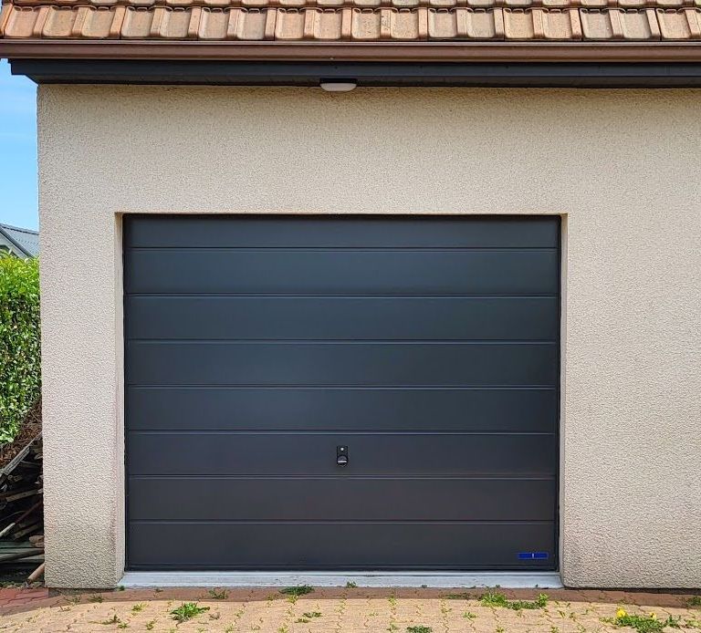 Porte de garage grise dans un bâtiment en stuc beige avec un toit marron.