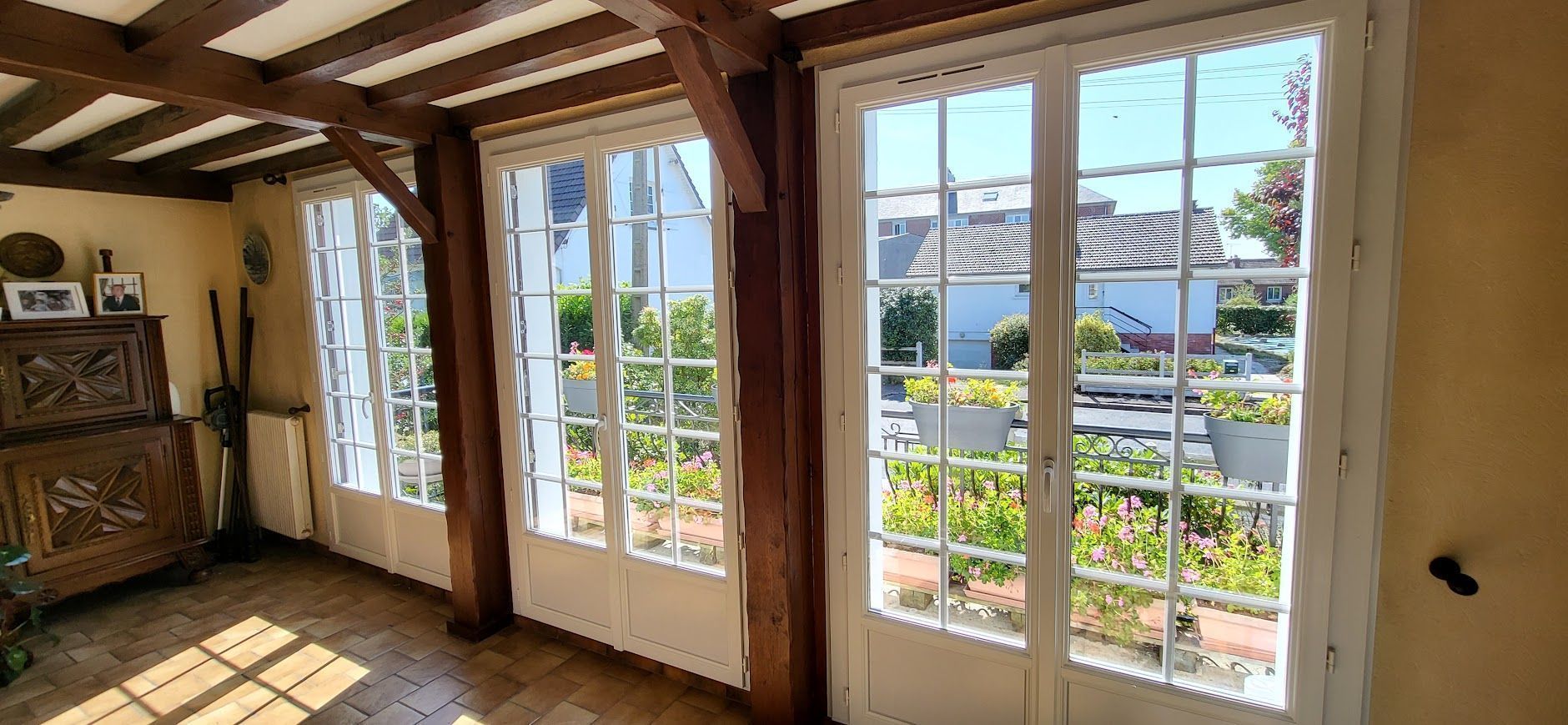 Intérieur avec fenêtres à cadre blanc, poutres en bois et vue sur la verdure et les maisons.