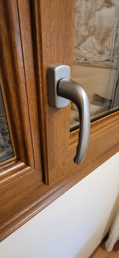 Gros plan sur une poignée de fenêtre. La poignée est argentée, le cadre est en bois brun.