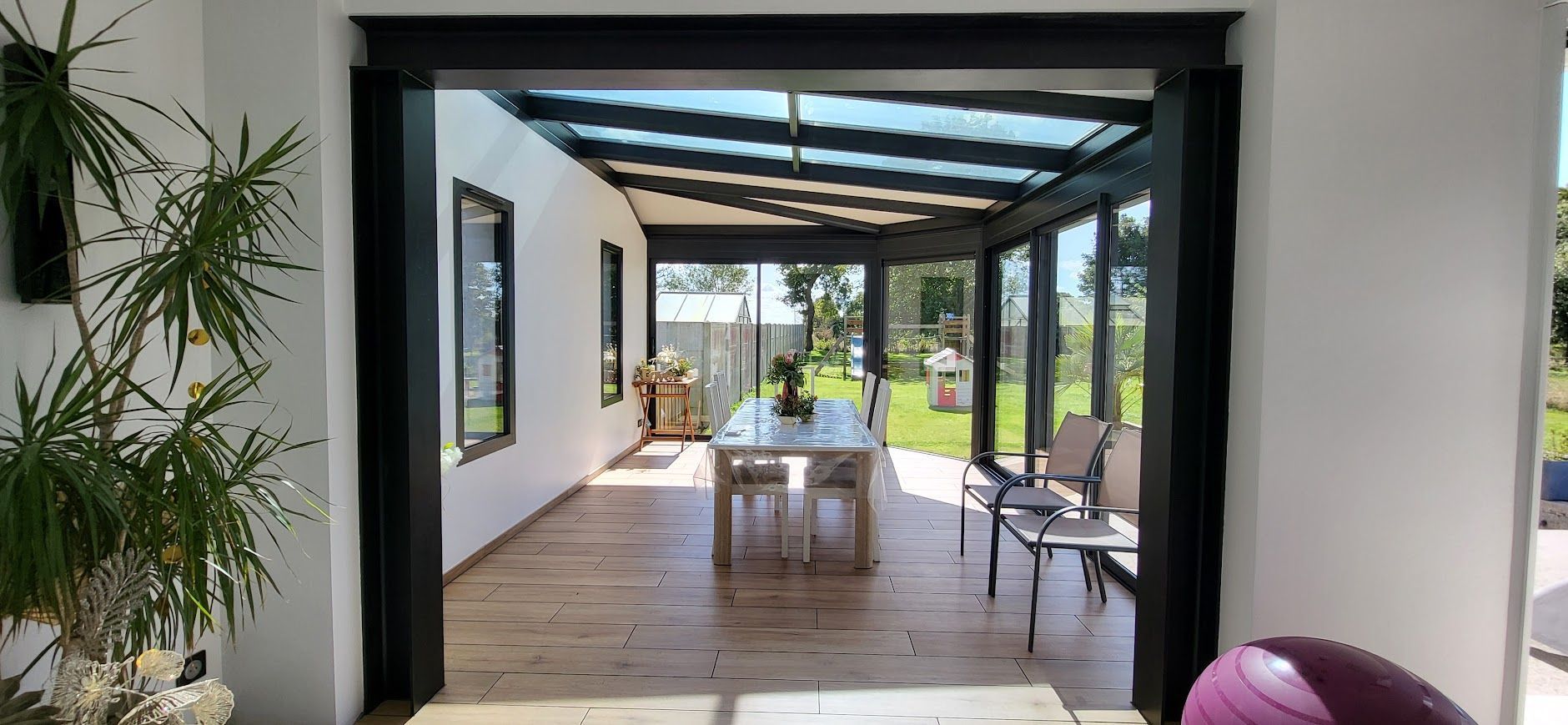 Une véranda avec une table et des chaises, donnant sur un jardin verdoyant.