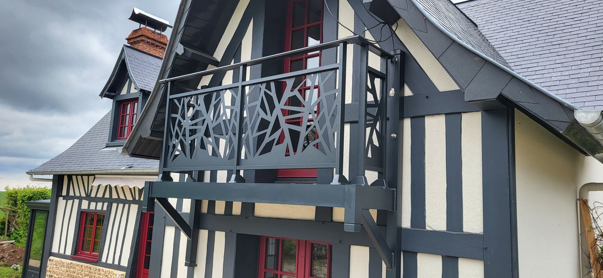 Maison à ossature bois noire et blanche avec un balcon doté d'une rambarde décorative en métal.